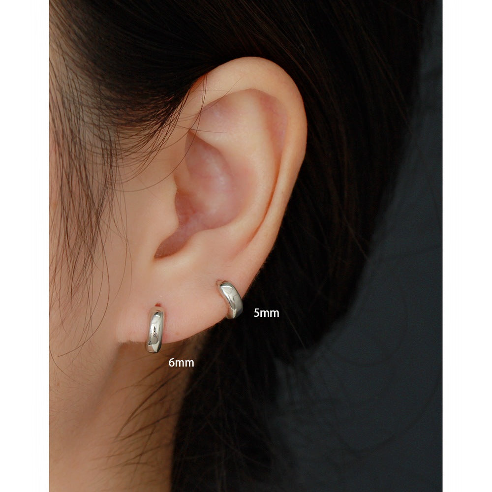 Close-up of an ear wearing two silver hoop earrings with size labels.