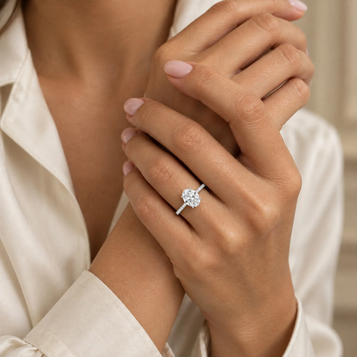 Oval moissanite pavé engagement ring styled on a woman’s hand with nude manicure