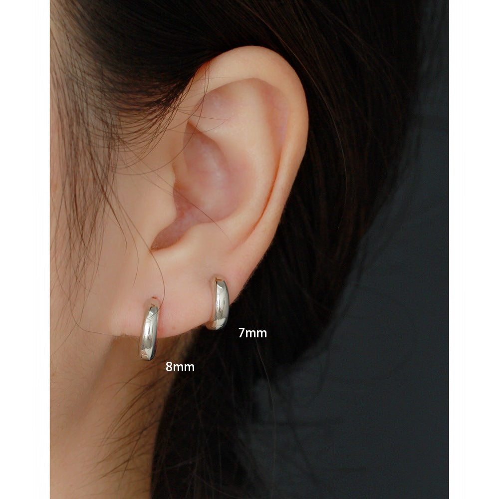 Close-up of an ear wearing silver hoop earrings with size labels.