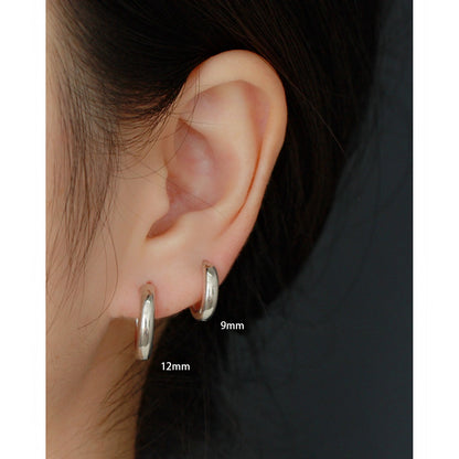 Close-up of an ear wearing two silver hoop earrings with size labels.