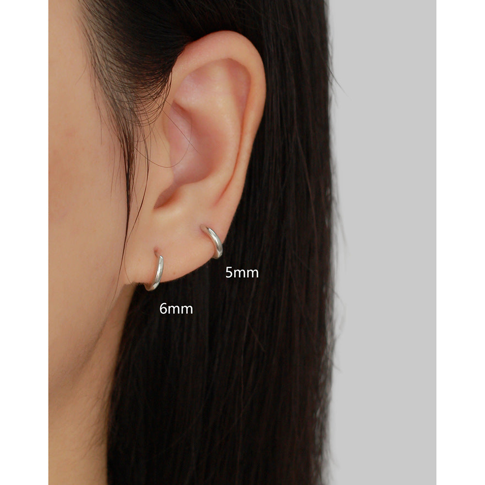 Close-up of an ear wearing two silver hoop earrings with size labels.