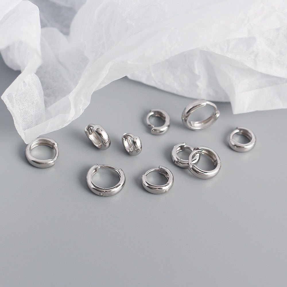 Set of silver hoop earrings on a light gray surface with white fabric in the background