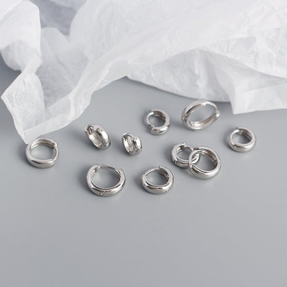 Set of silver hoop earrings on a light gray surface with white fabric in the background
