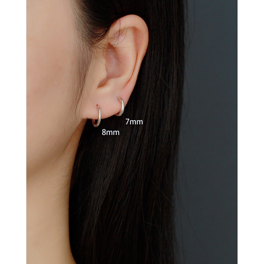 Close-up of an ear wearing a small hoop earring with size labels on a plain background