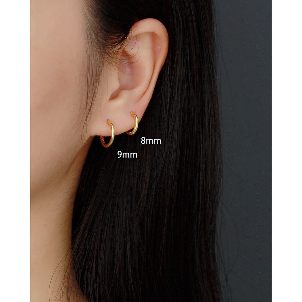 Gold hoop earrings worn by a person with text indicating size on an ear and dark background