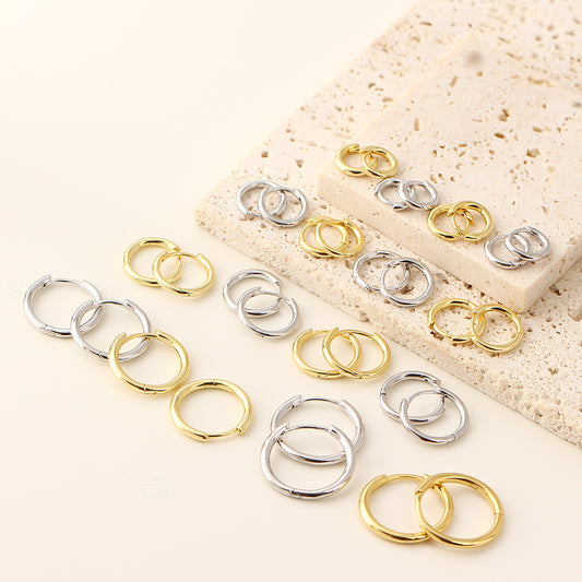 Gold and silver earrings on a textured beige surface
