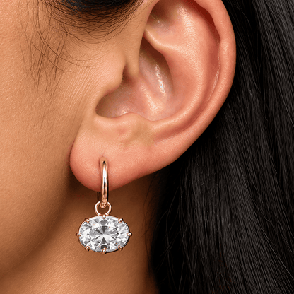 Close-up of an east-west oval moissanite drop earring with a gold-tone hoop on a brunette model