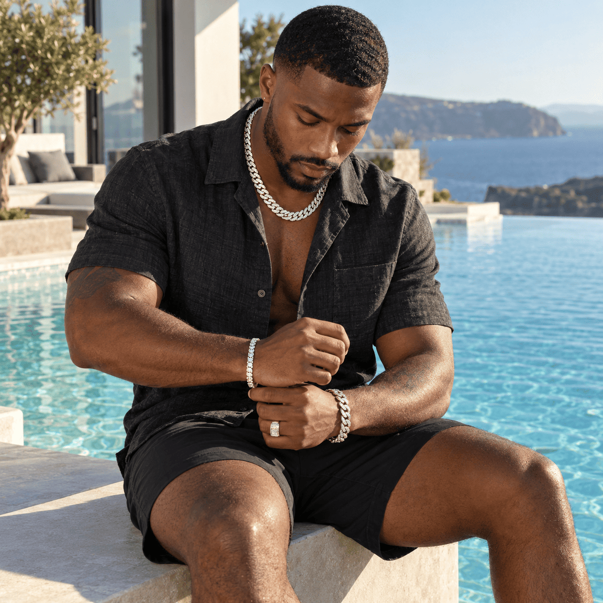 Man wearing ANNXMEE moissanite Cuban link chain, tennis bracelet, Cuban bracelet and statement ring by a luxury pool.